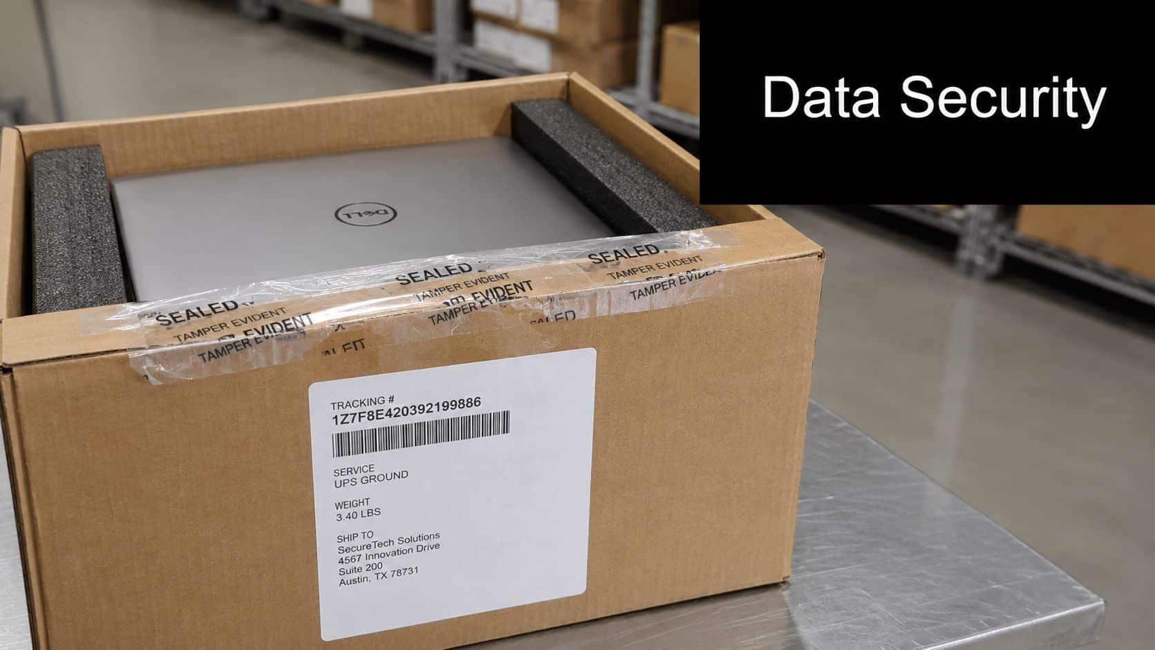 A Dell laptop secured in a shipping box with tamper evident tape on a packing table.